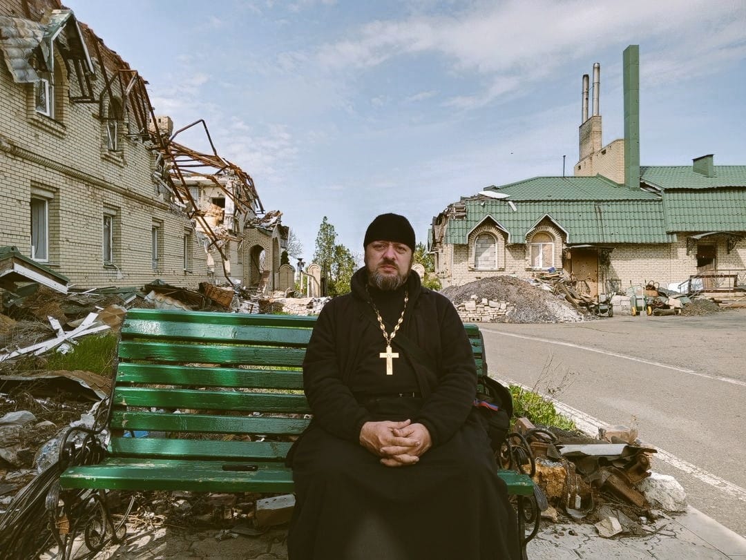 Hieromonk Feofan against the backdrop of the monastery destroyed by war